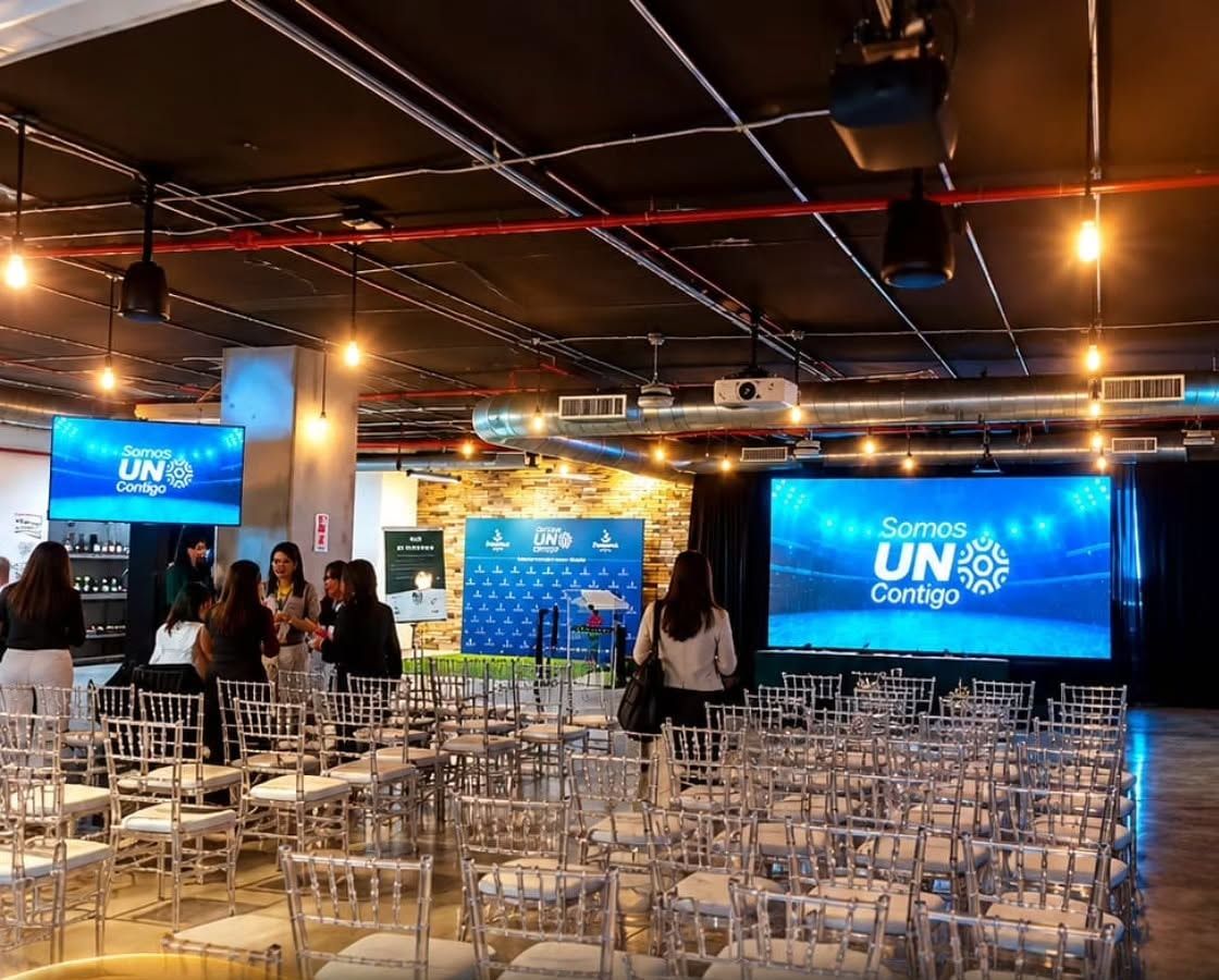 Salón corporativo con sillas, pantalla LED principal y pantallas laterales