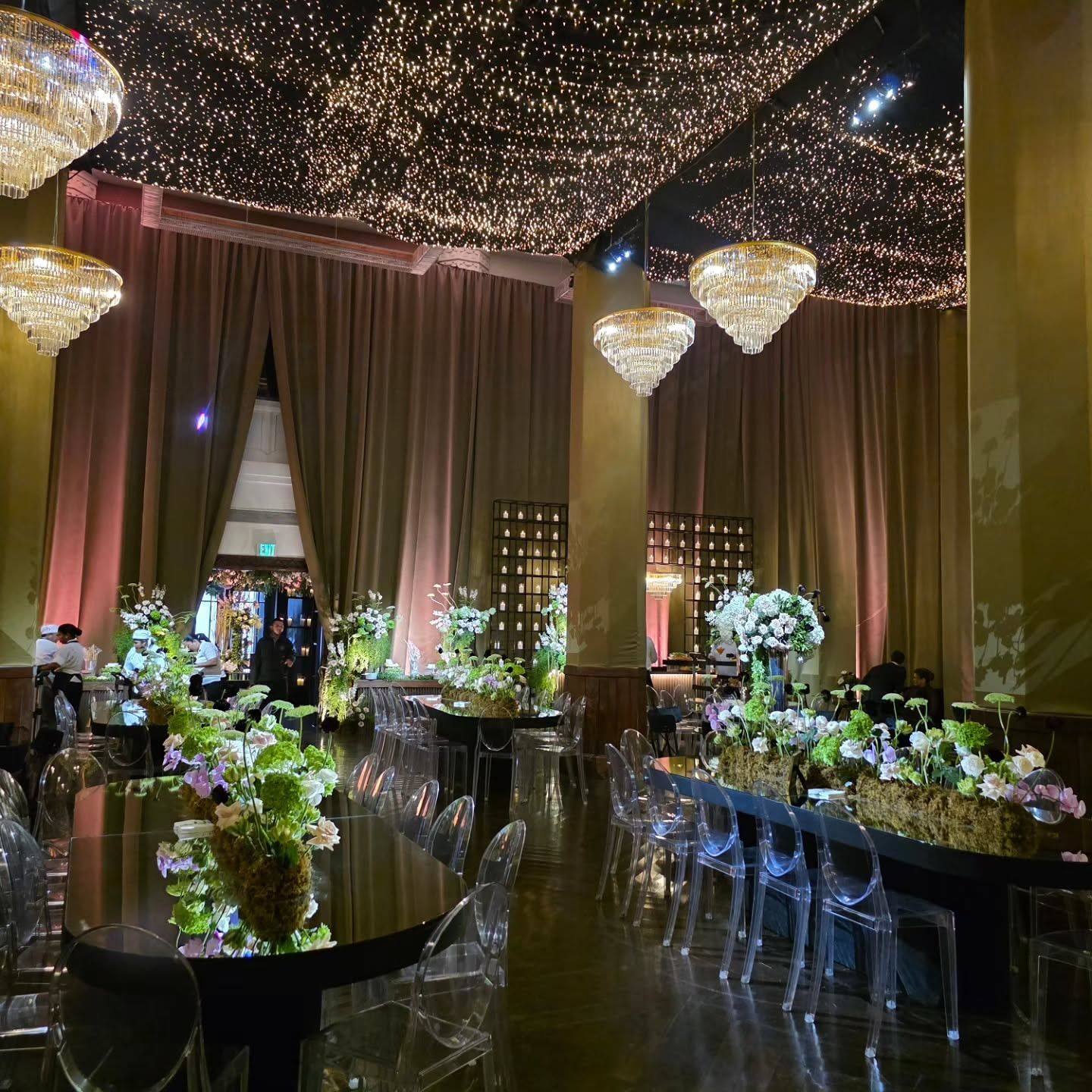 Salón con techo de luces, candelabros de cristal y mesas con flores
