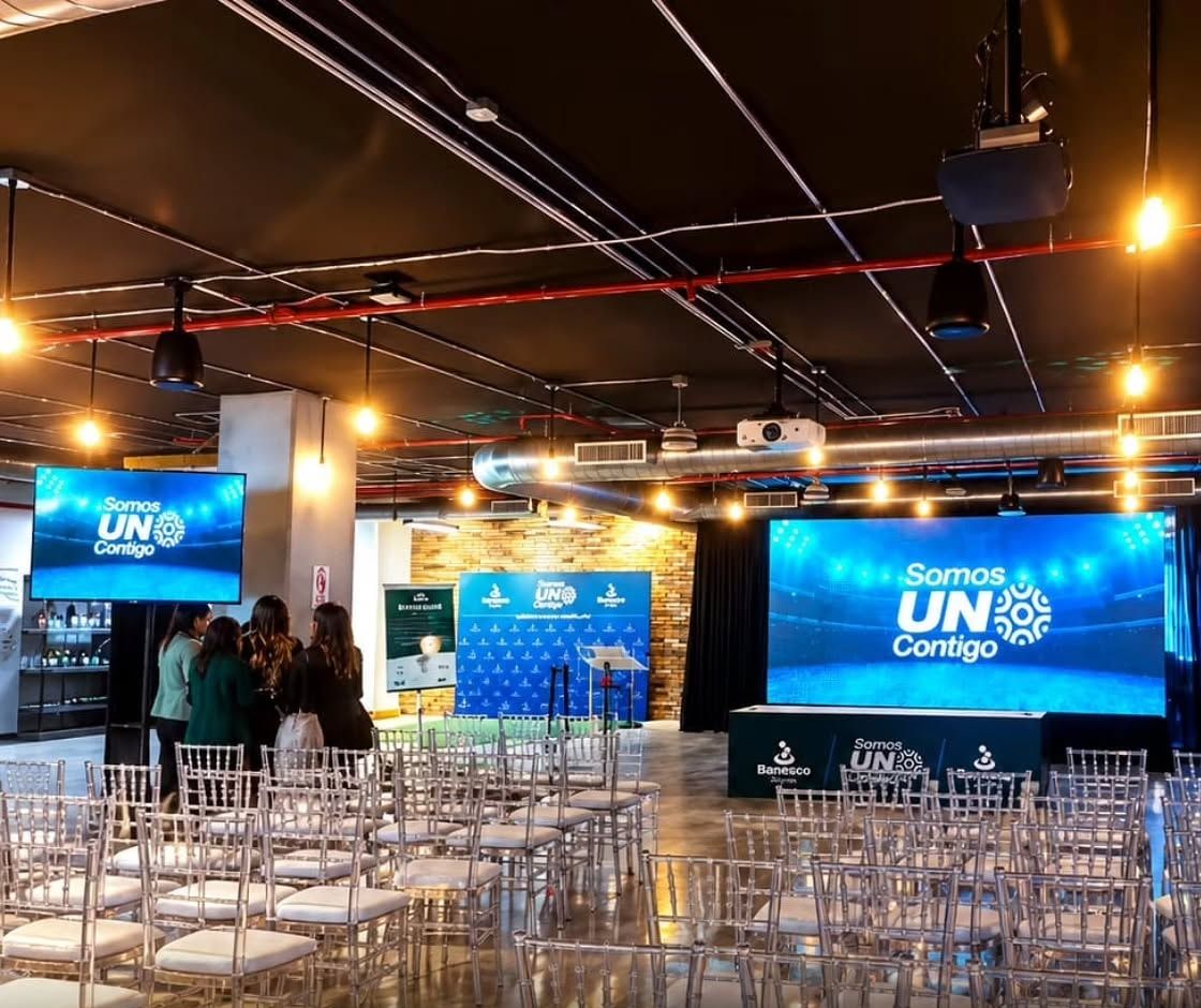 Asistentes llegando a un salón con pantallas LED y luces colgantes