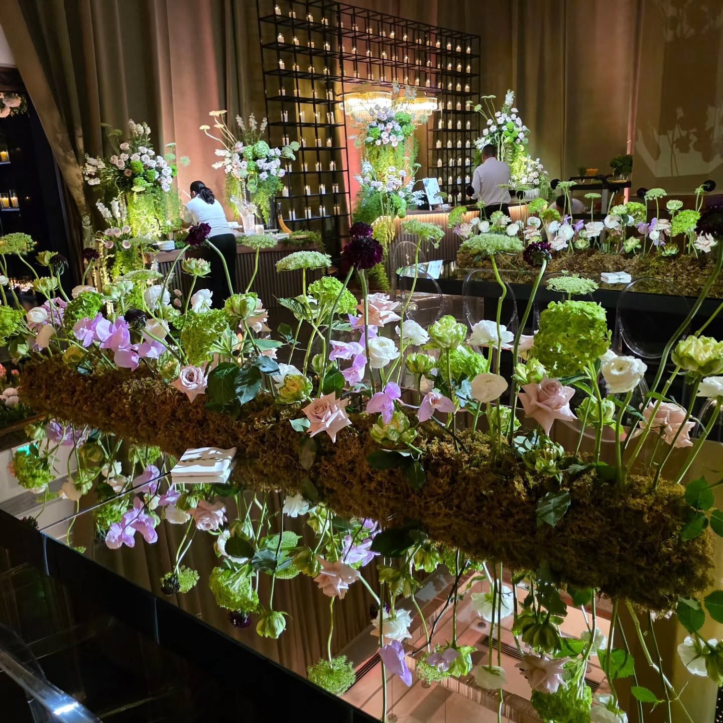 Centro de mesa de musgo y flores iluminado sobre una mesa larga
